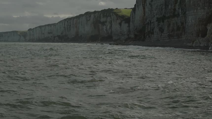 A person is swimming in a sea near a coast with huge stone walls