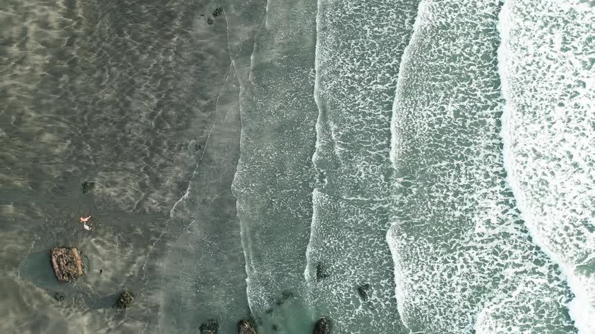 Two people walk along a beach as the surf comes in