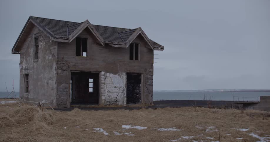 An abandoned hallowed out house sits under a cloudy sky