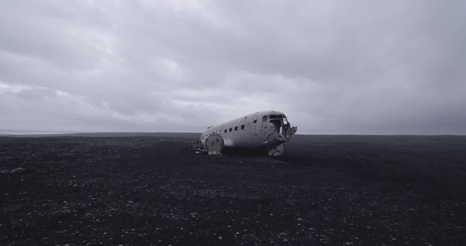 A wrecked airplane cabin sits in a rocky terrain on an overcast day