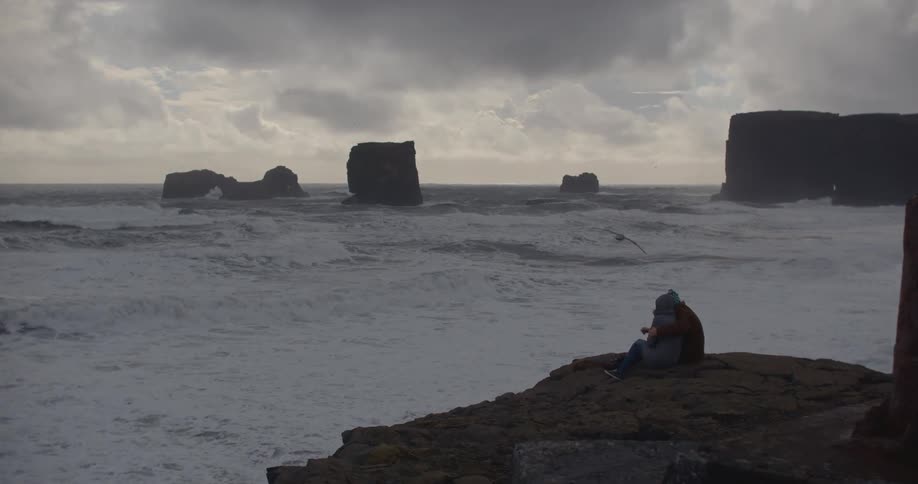 Large bird flies near couple seated on a large rock formation