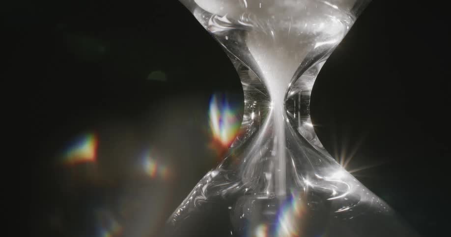 Closeup on a glass time vial with shining sand falling down