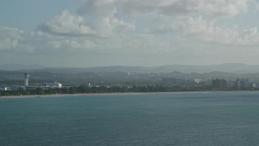 A coastal cityscape with mountains in the background under a partly cloudy sky