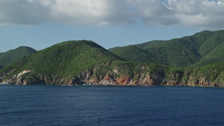 Green vegetation covers coastal hillside on partly cloudy day