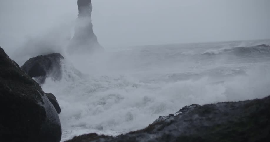 Large waves crash against the rocks of the shore