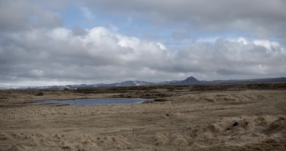 Large white fluffy clouds over a valley with a small body of water