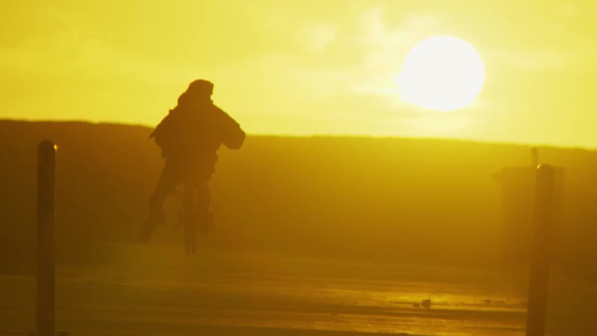 Cyclist starts pedaling bicycle while silhouetted against sunlight shining from sun in red sky