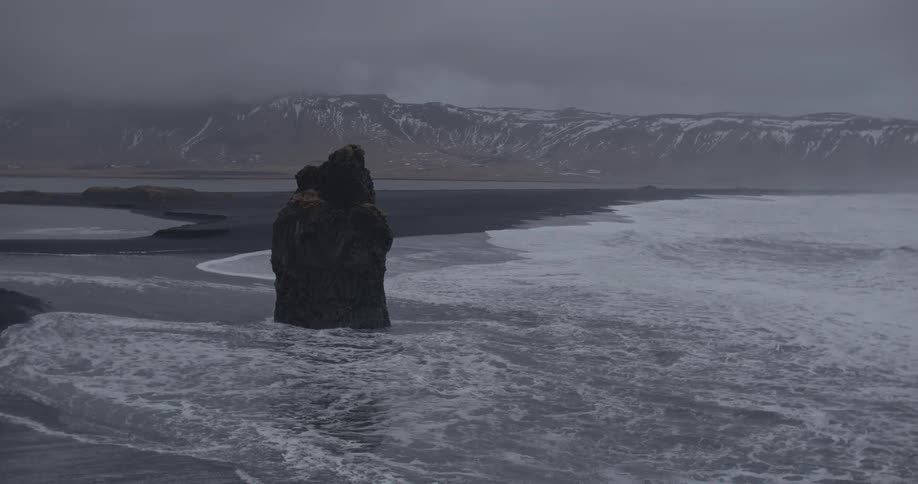 Waves roll past a monolithic rock onto a beach along a mountain shoreline