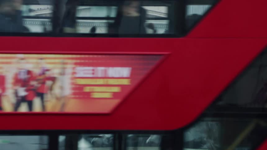 Statue of two lions in front of a museum with a red public bus passing in front