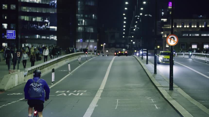 Person riding a bike in the midst of a busy street with pedestrians and vehicles at night