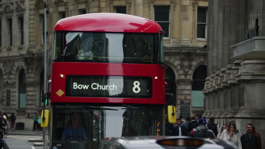 A red bus traveling in the city of london during a cold day