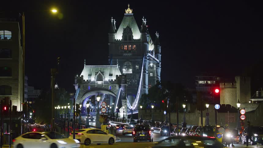 A busy street at night with vehicles and people and in the background a bridge and a castle