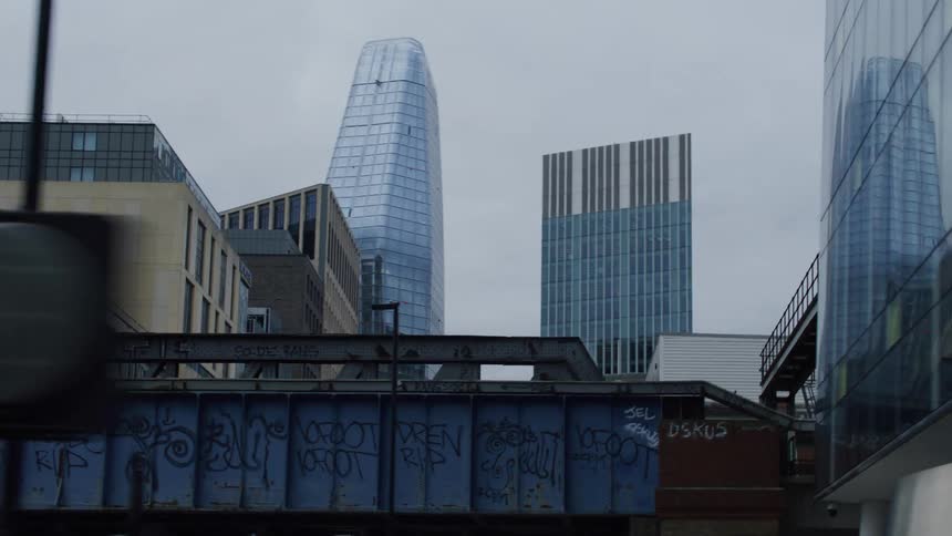 Large sky scrapers tower over a graffiti covered bridge on a cloudy day