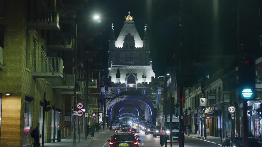 Busy night street with vehicular and pedestrian traffic and ahead a bridge with a structure