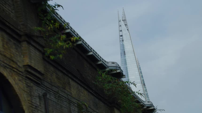 An old building with dark bricks and a sloping roof contrasted with a modern skyscraper with a pointed top