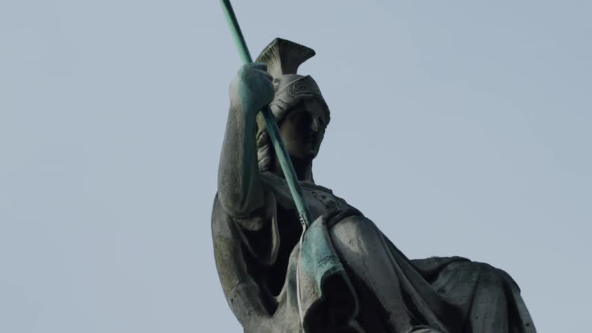Statue of a warrior on top of an ancient building in the middle of a metropolis
