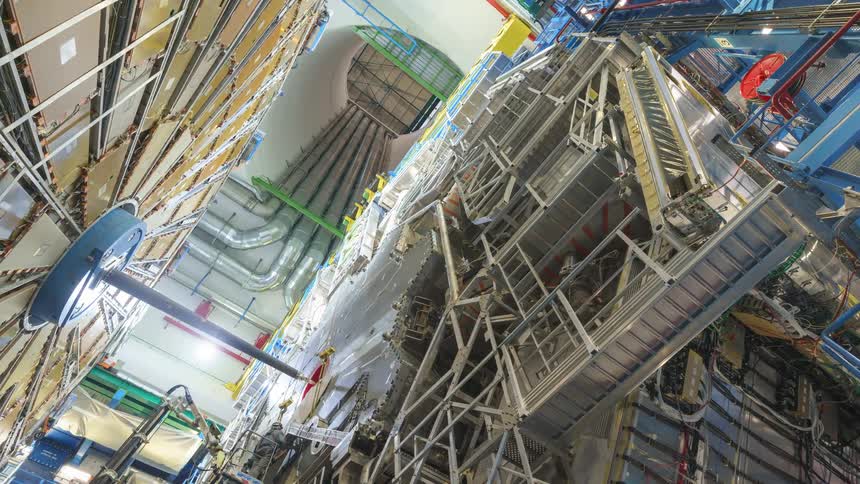 Workers use crane to construct large paneled object in cavernous room with large shaft leading upward