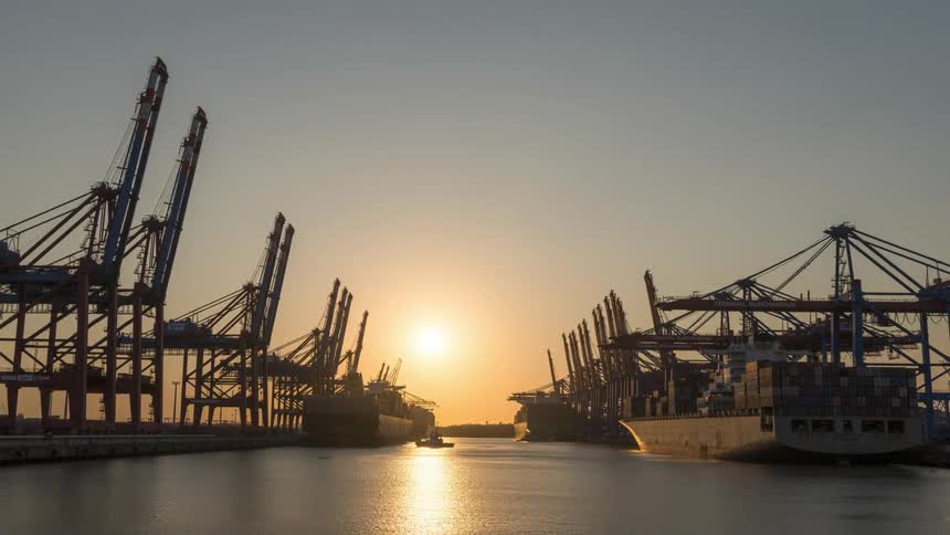 Panorama of boats docked in a harbor with containers and the sun rising on the horizon in timelapse