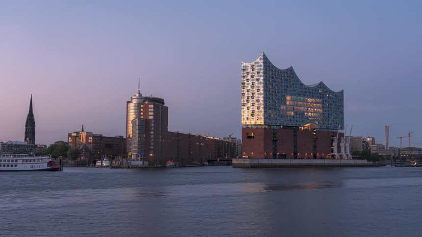Buildings by the sea with boats passing by as the day turns into night in timelapse