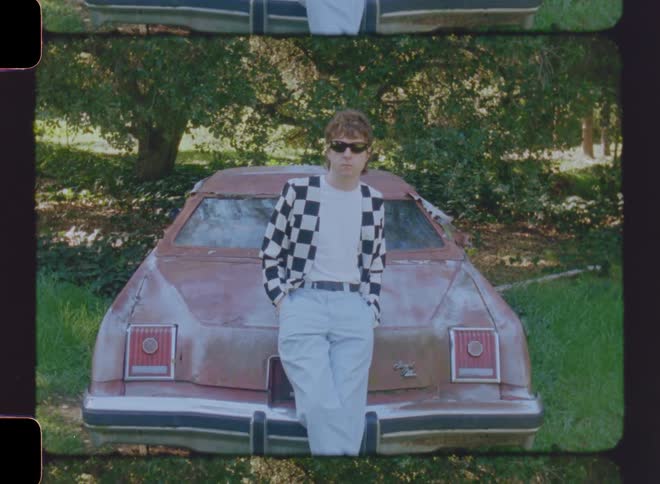 Man with sunglasses posing while leaning on the trunk of a vintage car