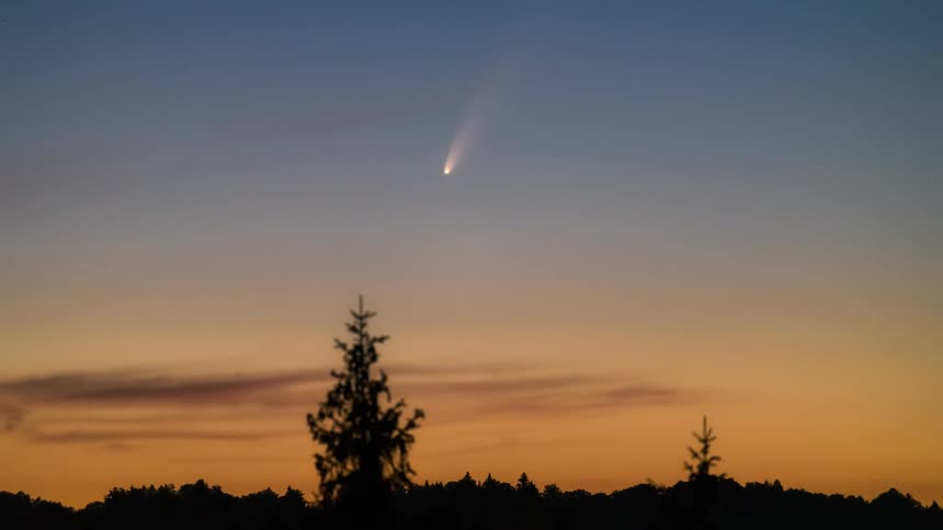 A large comet moves across a partially lit sky