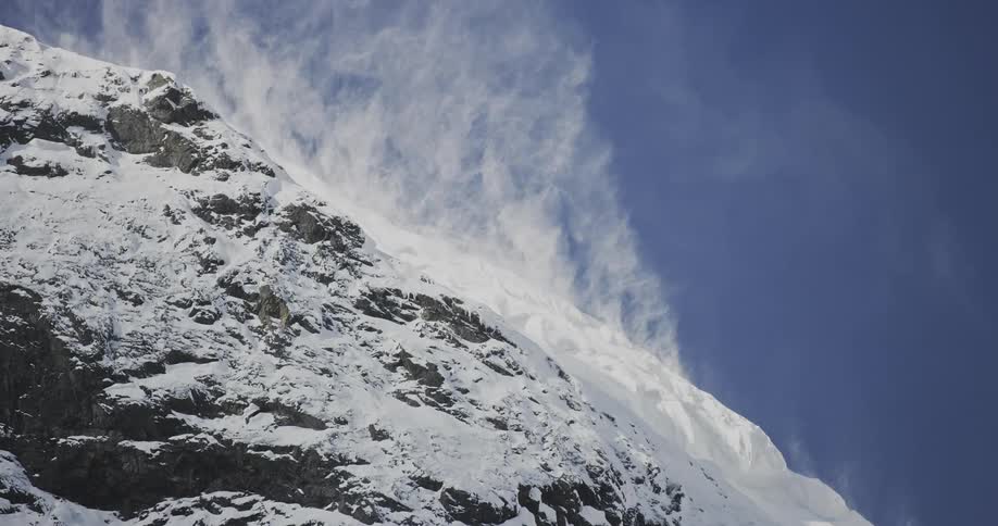 The wind blows snow on a mountain top in a clear sunny day