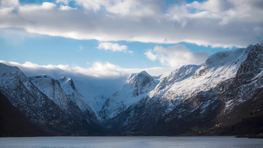A lake surrounded by mountain covered in snow on a sunny day