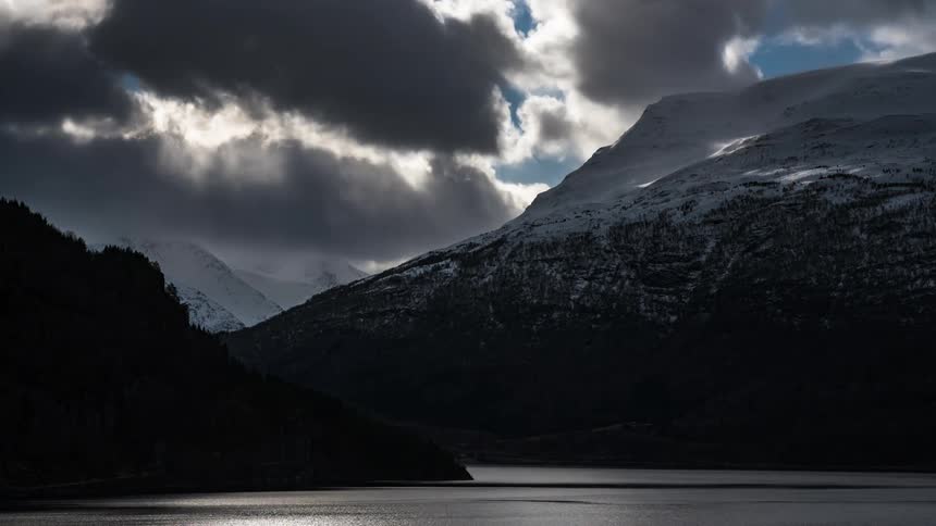 Clouds passing over the mountains in timelapse in front of a fjord