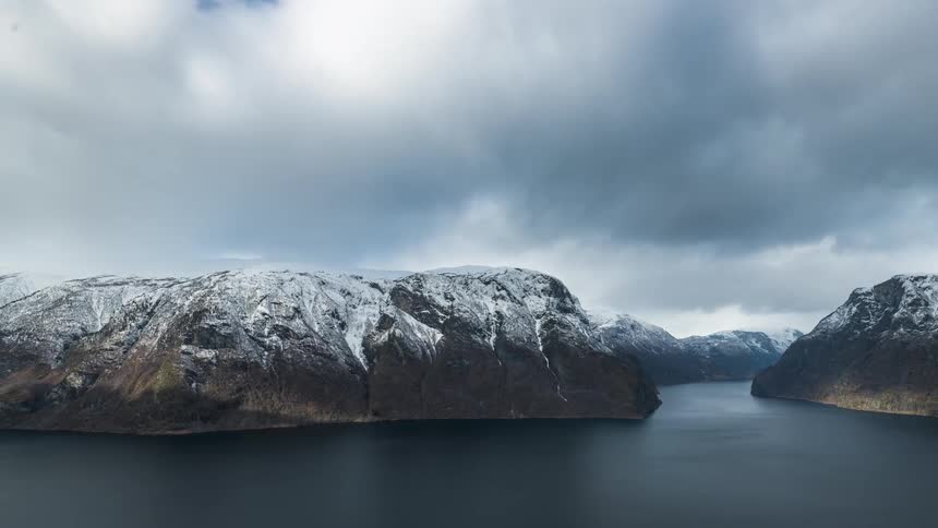 A river surrounded by snowcapped mountains under a partly cloudy sky