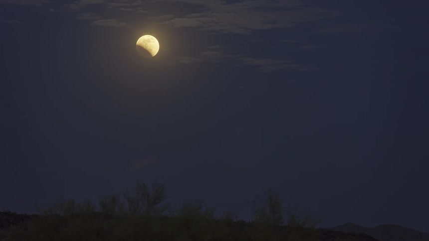 A moonlit sky and clouds with a dark landscape below