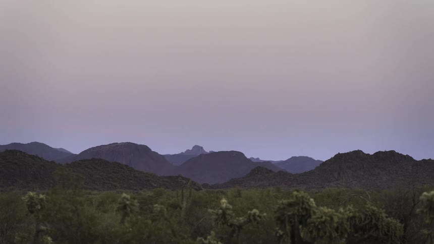 Desert at dawn or dusk with silhouettes of cacti and rugged mountains