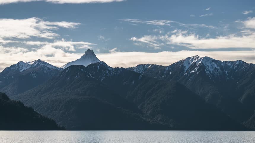 clouds moving over a mountain range by a lake