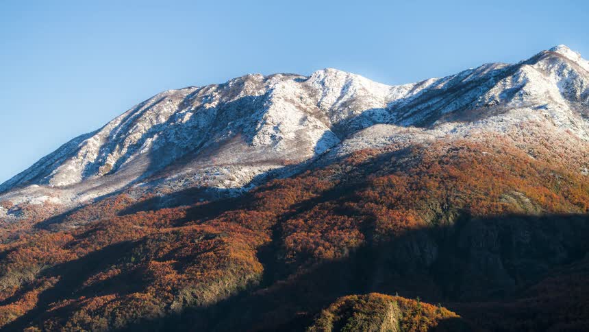 Retreating shadows revealing mountains covered in snow and fall colors