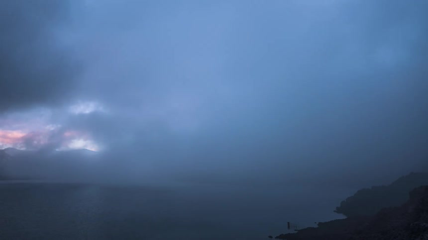 Heavy clouds flow over the mountains and lake