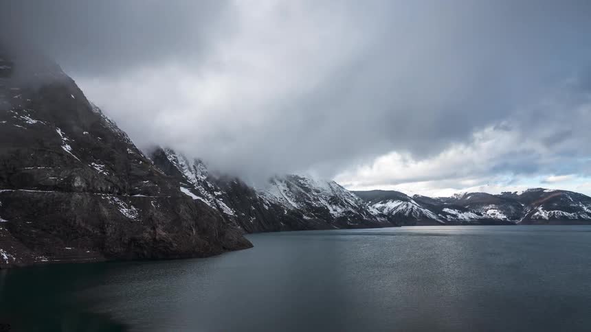 Time lapse cloud movement over winter mountain range and lake