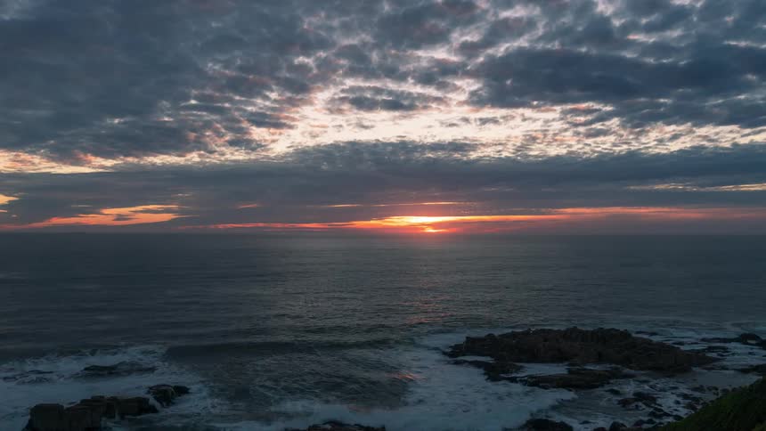 The sun sets near the horizon and over the ocean