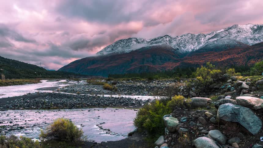 snowy mountains and a stream with clouds during sunset