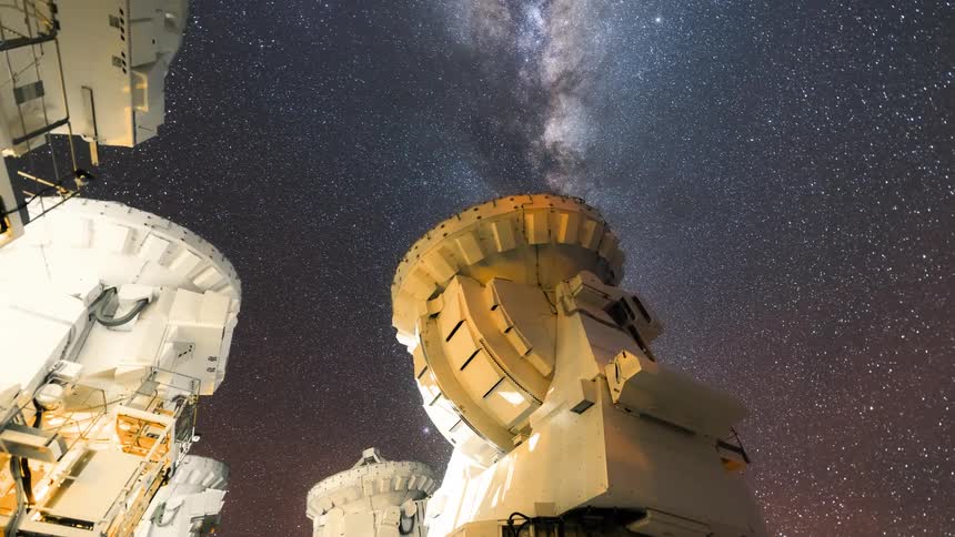large radio telescopes moving during the night with the bright milkyway galaxy moving overhead
