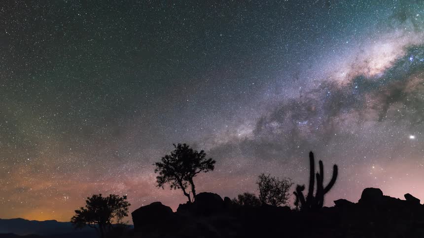 The milky way galaxy moves through the sky over a desert environment