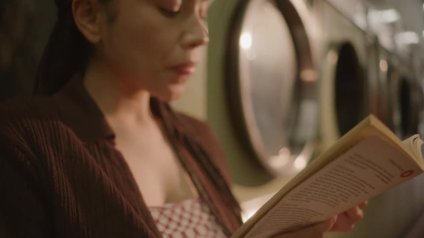 A woman reading a book in a laundromat