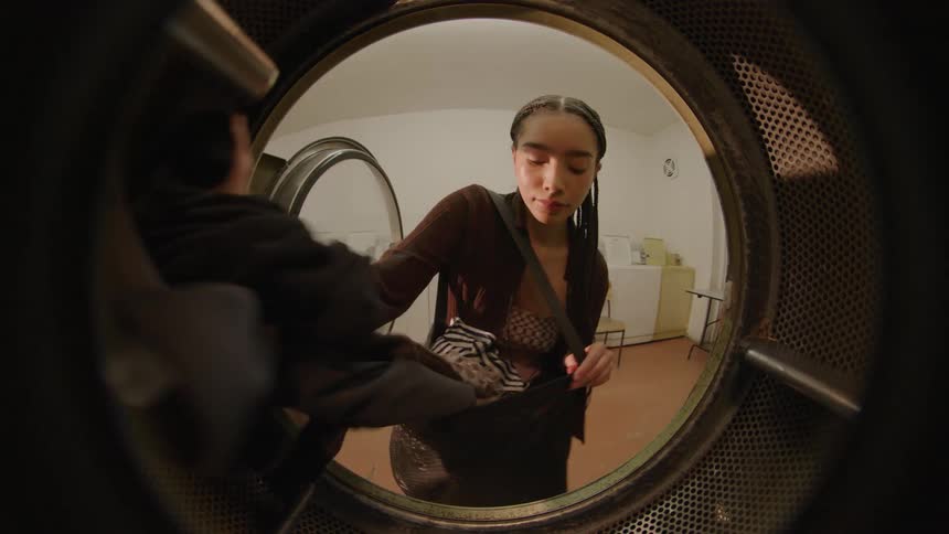 A young woman puts clothing in a washing machine