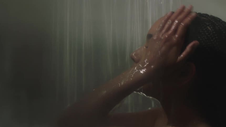 Close up shot of a woman showering, washing her hair, through foggy glass shower door