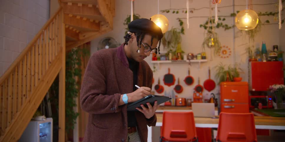 Man indoors taking notes with a pen on his tablet