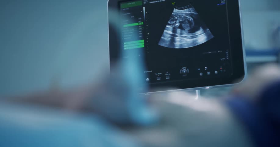 Closeup of a womans hand holding a device over a pregnant womans belly and seeing the baby on a multimedia