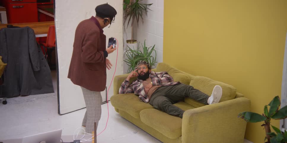 A person taking a photo of someone lying on a yellow couch in a bright room