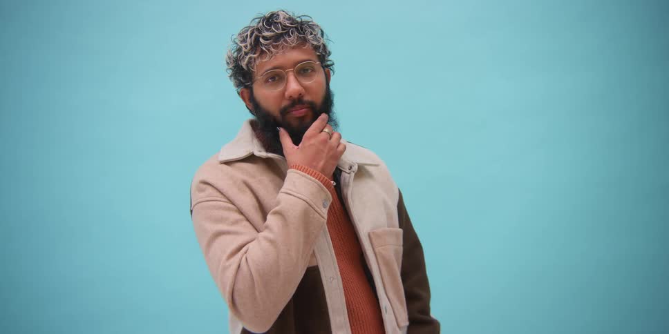 A man posing for a fashion shoot against a blue wall background