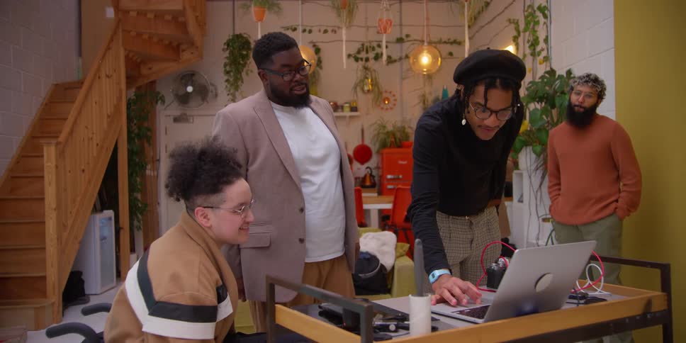 Four men talk while looking at a laptop