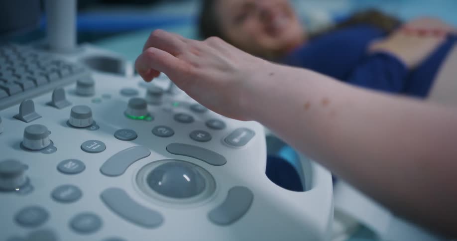 Doctor using a medical device and passing it over the belly of a smiling pregnant woman