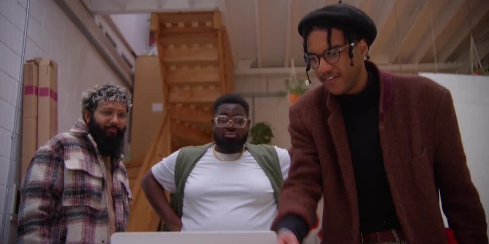 Three men laugh while looking at a laptop