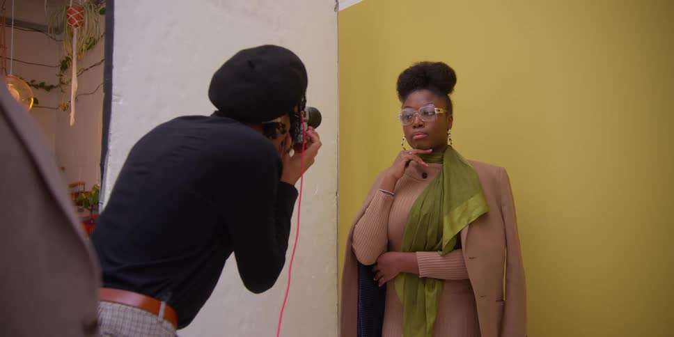 A black woman strikes a pose for a man with a camera